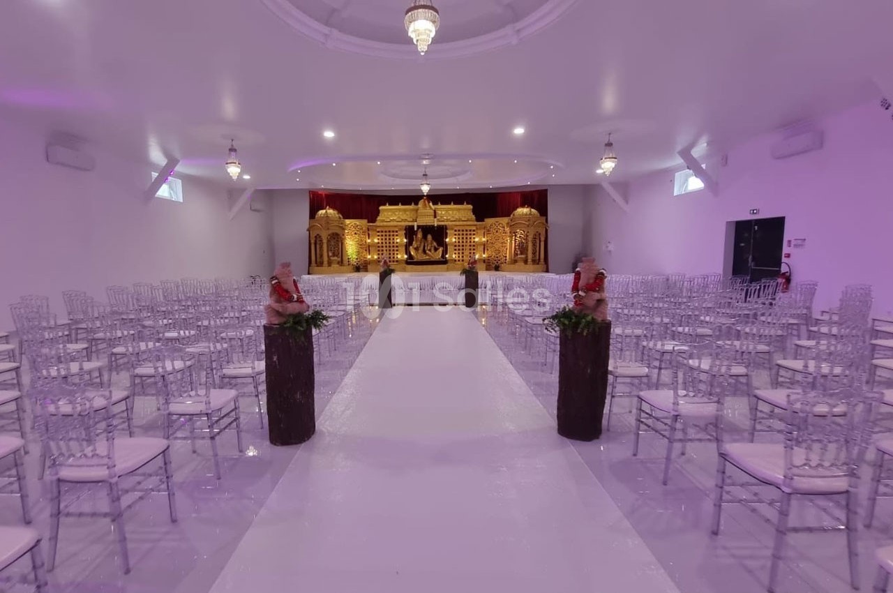 Salle de réception décorée avec des chaises transparentes, une allée centrale blanche et une scène ornée de dorures.
