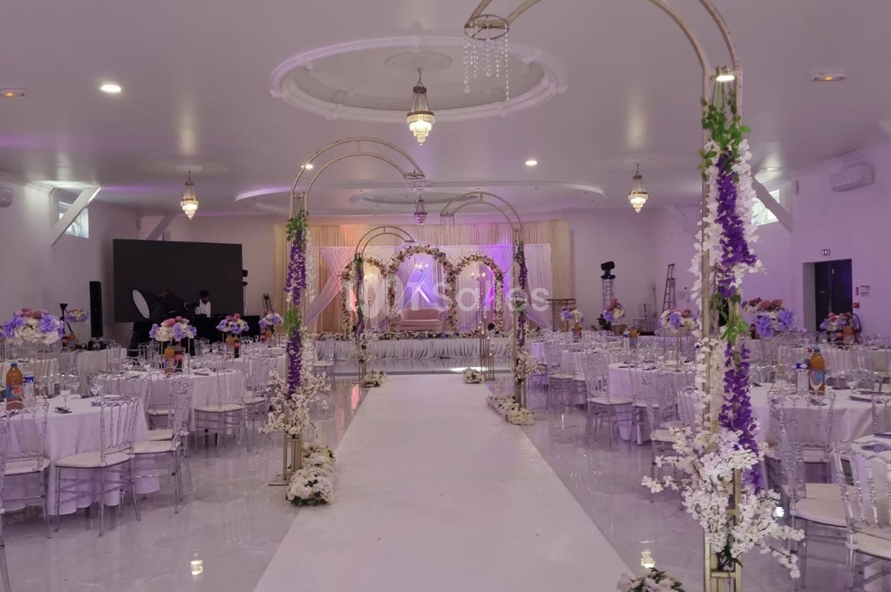 Salle de réception décorée avec des arches fleuries, tables dressées et éclairage tamisé pour un événement festif.