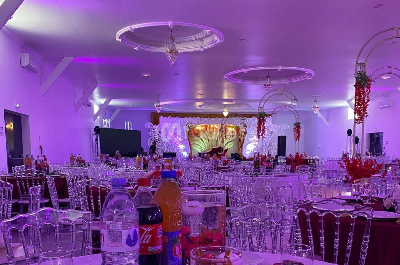 Salle de réception décorée avec des tables dressées, éclairage violet et une scène ornée en arrière-plan.