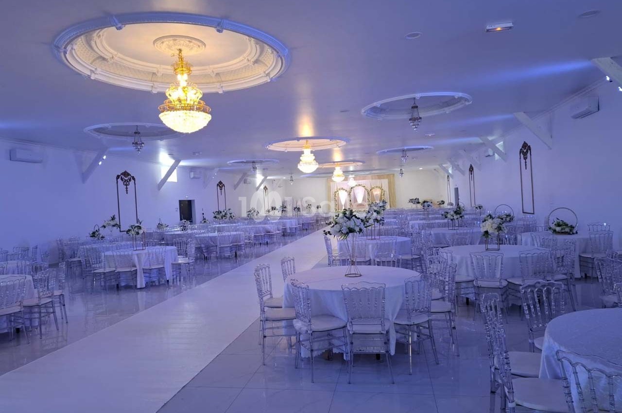 Salle de réception élégante avec tables rondes décorées, chaises transparentes et lustres suspendus.