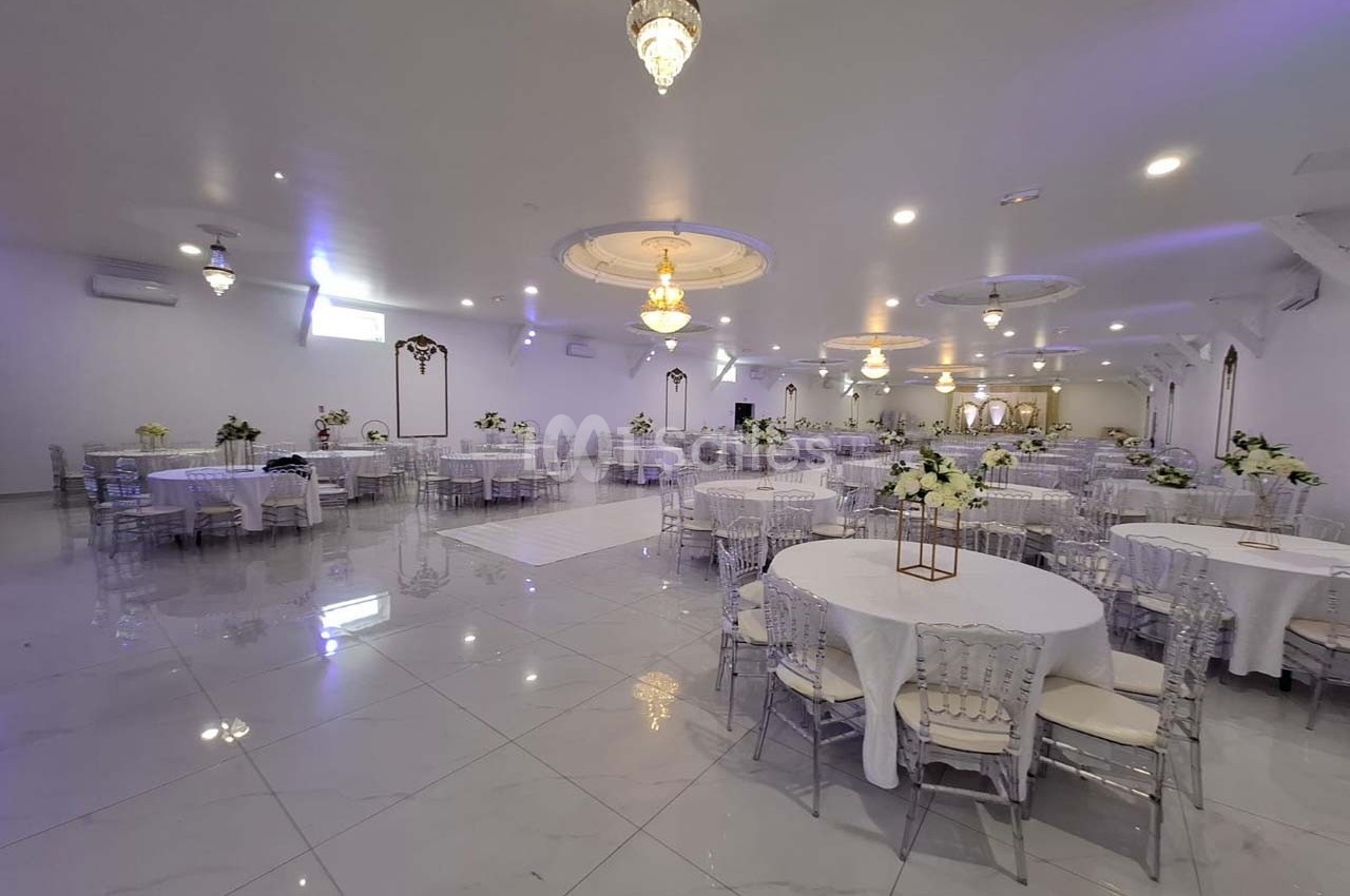 Salle de réception spacieuse avec tables rondes décorées de fleurs blanches et éclairage élégant.