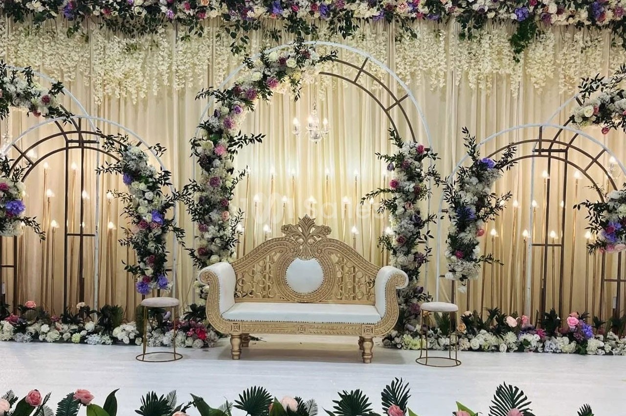 Décor de cérémonie avec un canapé doré, arches fleuries, rideaux beige et compositions florales colorées.