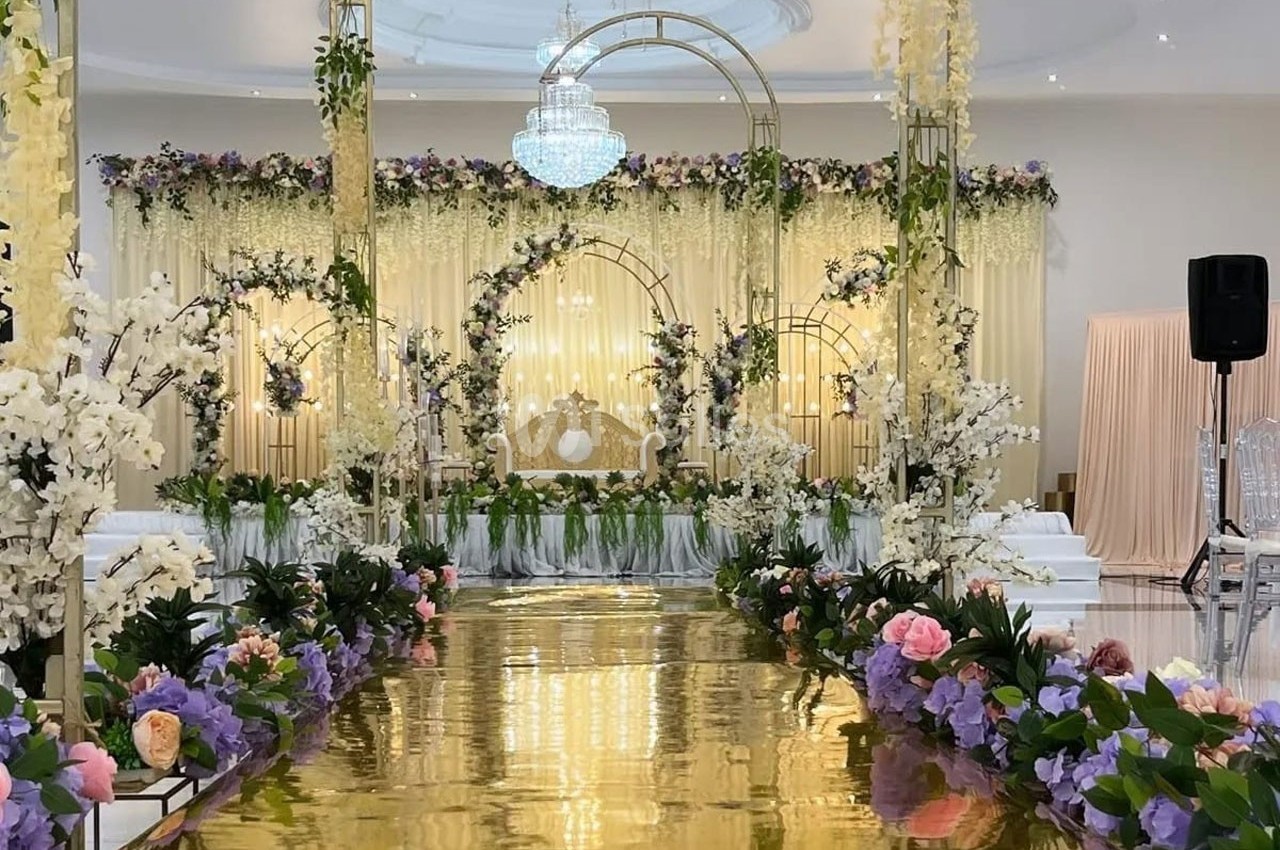 Allée dorée bordée de fleurs colorées menant à une arche décorée de guirlandes et d'un fauteuil dans une salle élégante.
