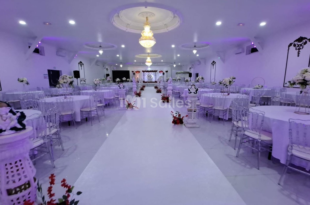 Salle de réception décorée avec des tables rondes, des chaises transparentes et des arrangements floraux sous un éclairage…