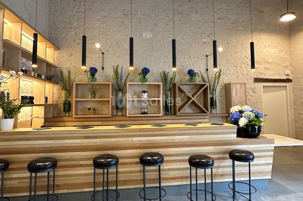 Un bar en bois clair avec des tabourets noirs, des étagères décorées de fleurs et un éclairage suspendu moderne.