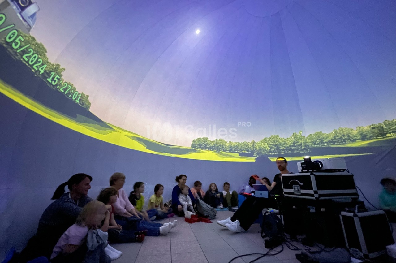 Des enfants et des adultes assis dans un dôme immersif observant une projection panoramique de paysage.