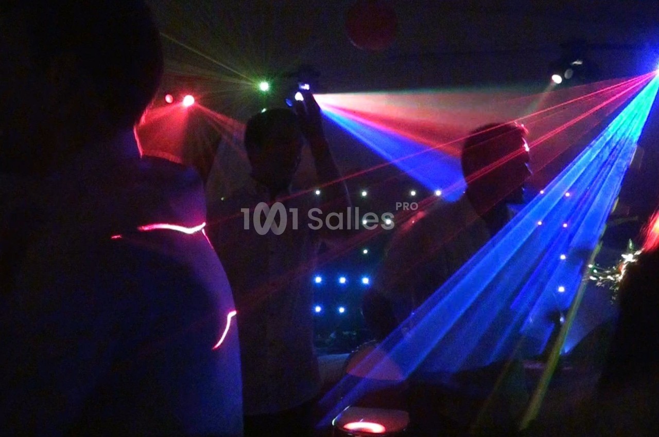 Personnes dansant sous des jeux de lumières colorées et des faisceaux laser dans une ambiance de fête nocturne.