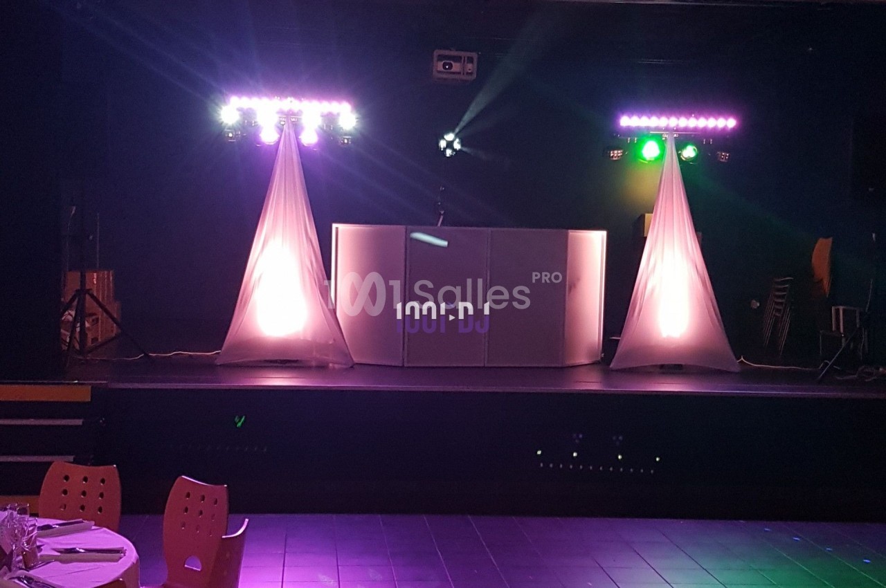 Installation de DJ sur une scène avec éclairage coloré, deux colonnes lumineuses et une table de mixage.