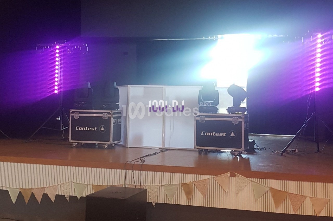 Installation de matériel de DJ sur une scène, avec éclairages violets et deux caissons de transport marqués ’Contest’.
