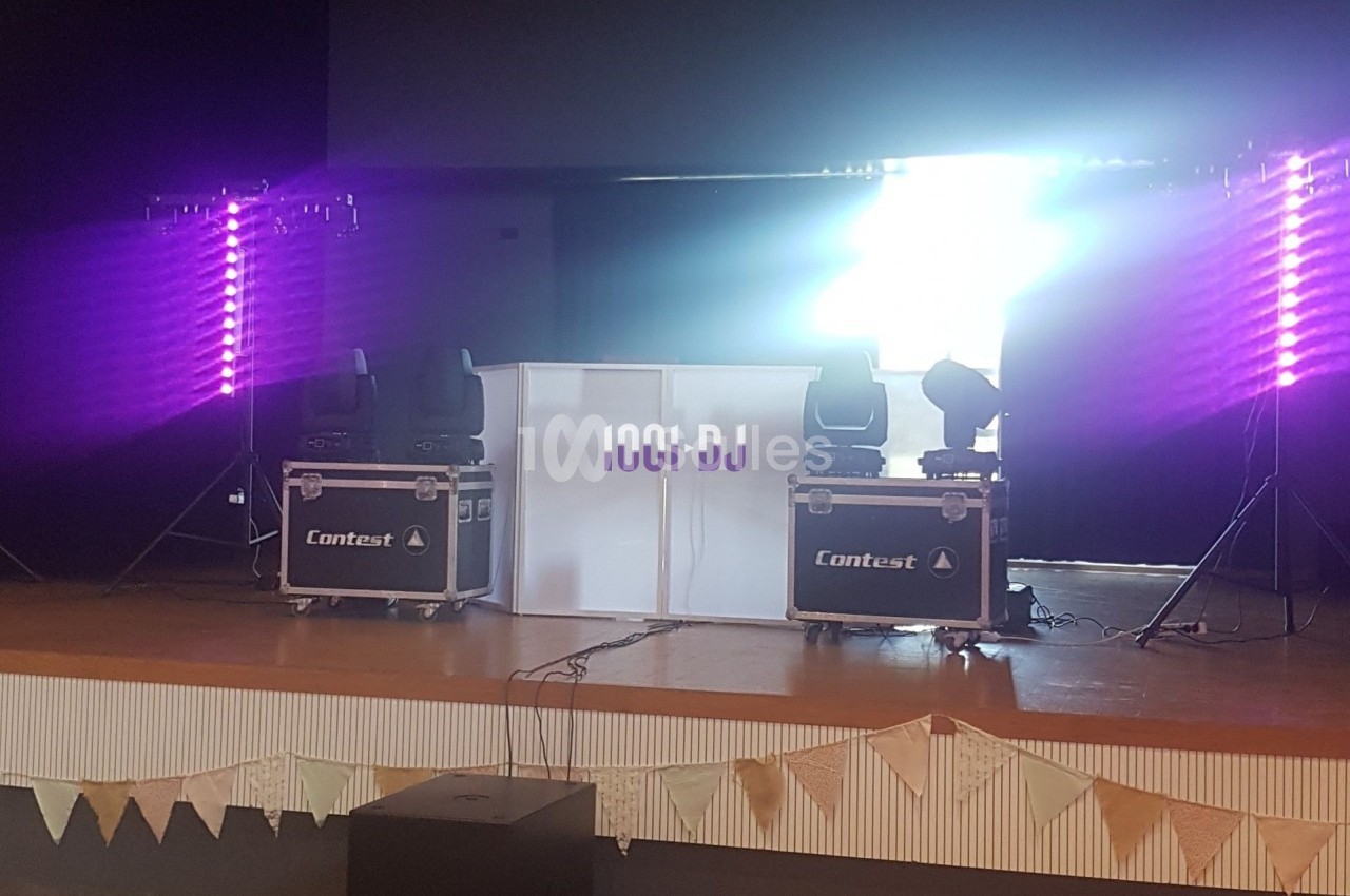 Installation de matériel de DJ sur une scène, avec lumières violettes et guirlandes décoratives en bas.