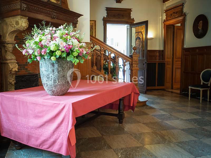 Vase de fleurs colorées sur une table recouverte d'une nappe rose, dans un intérieur élégant avec escalier en bois.