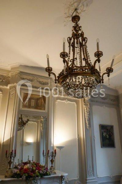 Lustre en métal doré orné de cristaux suspendu dans une pièce élégante avec moulures et cheminée décorée de fleurs.