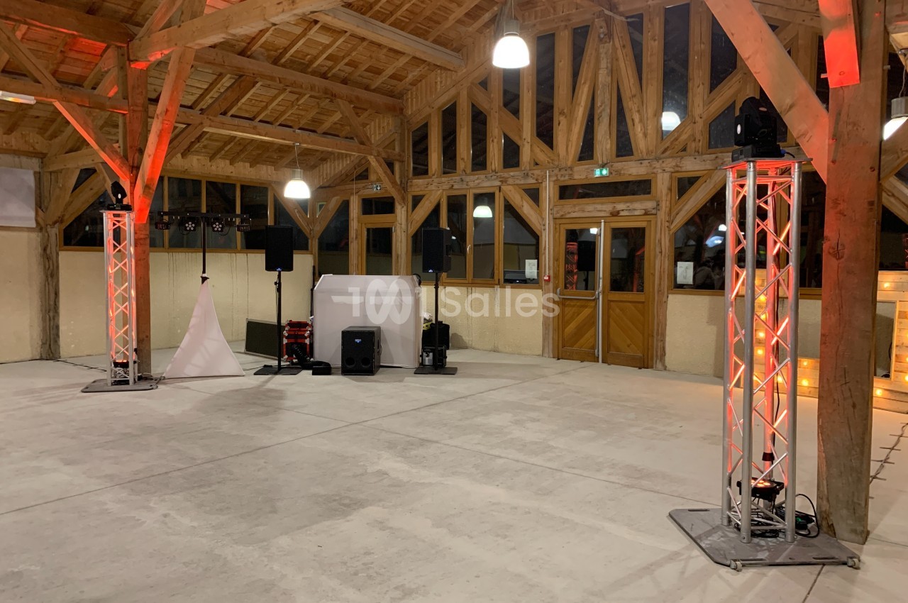 Grande salle en bois avec charpente apparente, éclairages rouges, matériel de sonorisation et espace vide au centre.