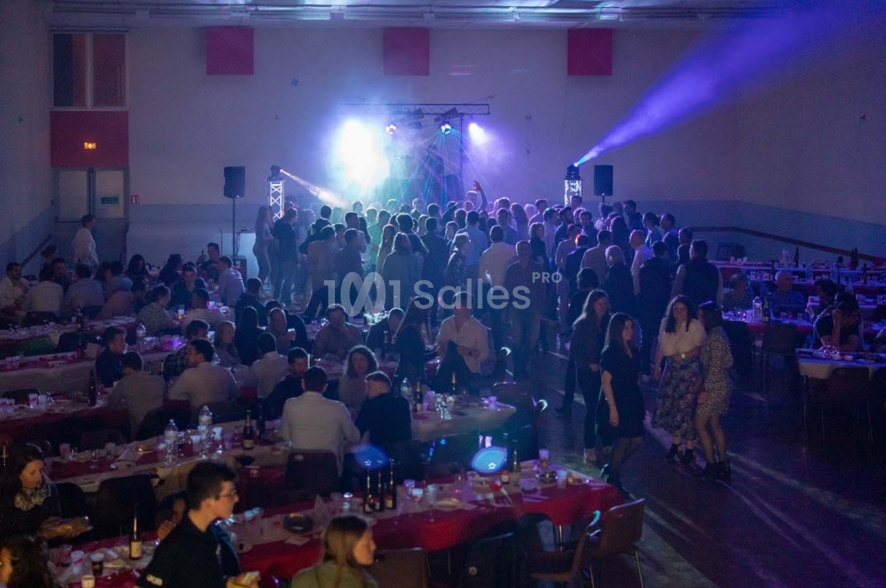 Salle de réception avec des tables dressées et des invités dansant sous des jeux de lumière sur une scène.
