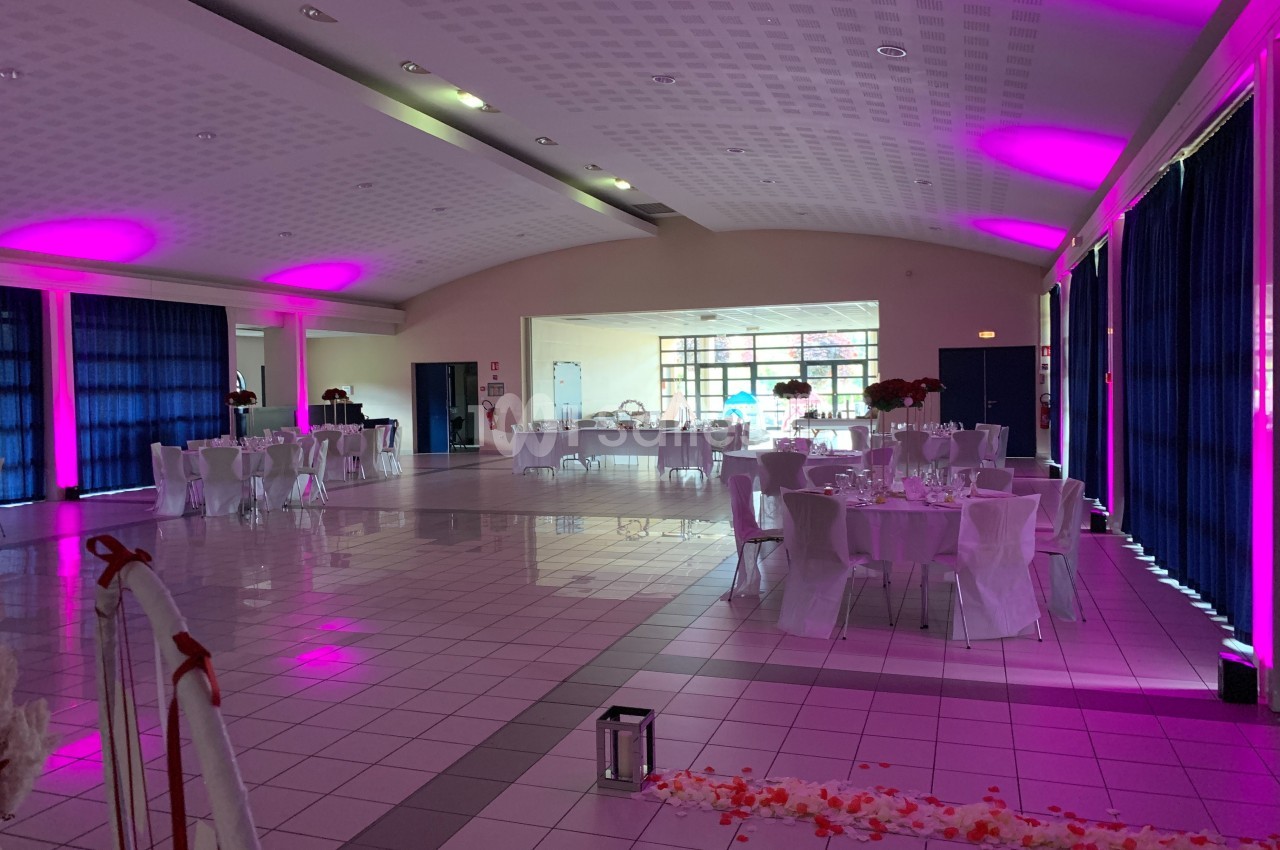 Salle de réception décorée avec des tables dressées, éclairage rose et rideaux bleus.