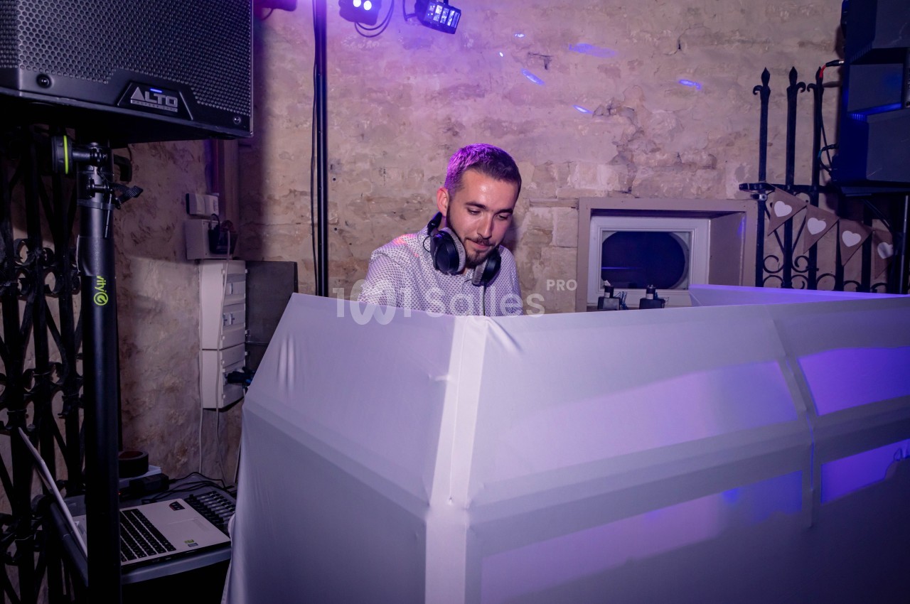 Un DJ mixant de la musique derrière une table éclairée, dans une salle en pierre avec des équipements audio.