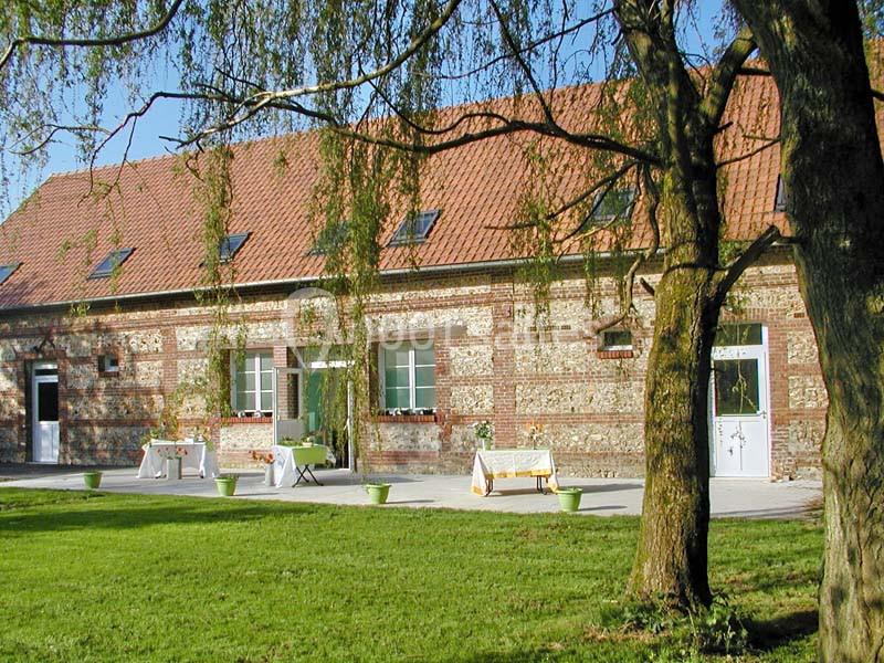 Bâtiment en briques avec toit en tuiles rouges, entouré d'une pelouse et d'arbres sous un ciel dégagé.