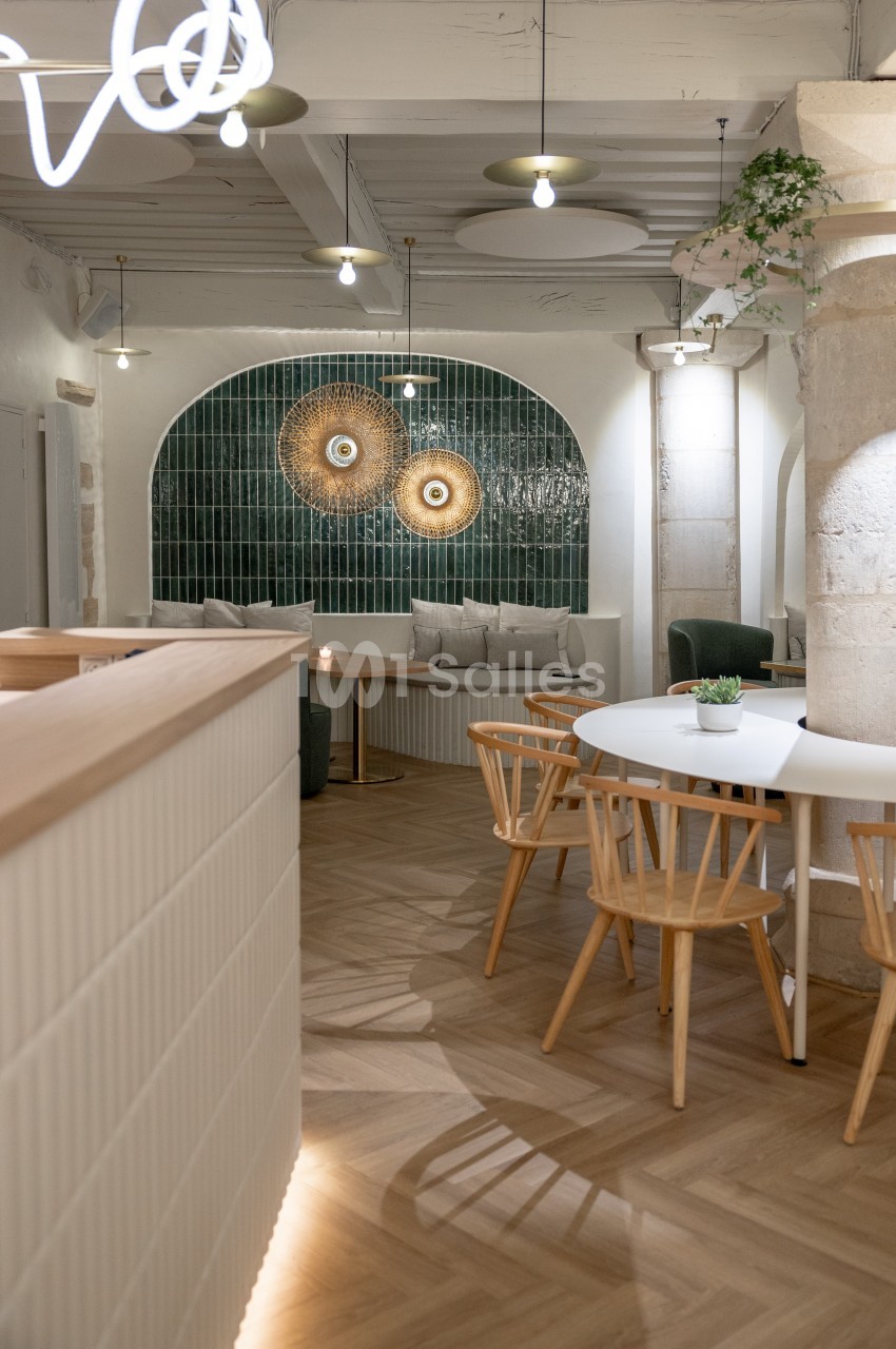 Intérieur d'un café moderne avec tables en bois, chaises design et mur décoré de carreaux verts et d'art mural.