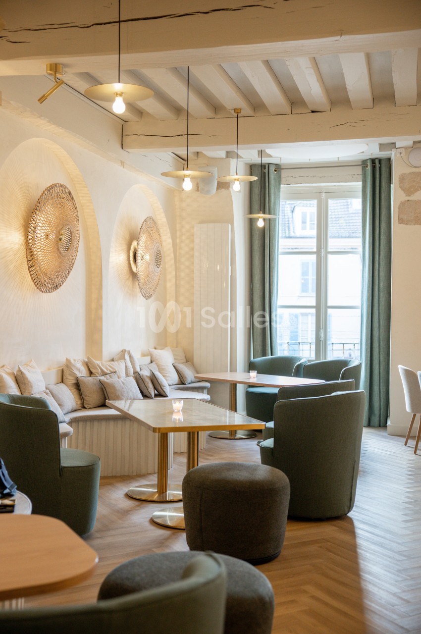 Espace lumineux avec tables, fauteuils verts, banquettes et décorations murales dans un intérieur moderne et épuré.