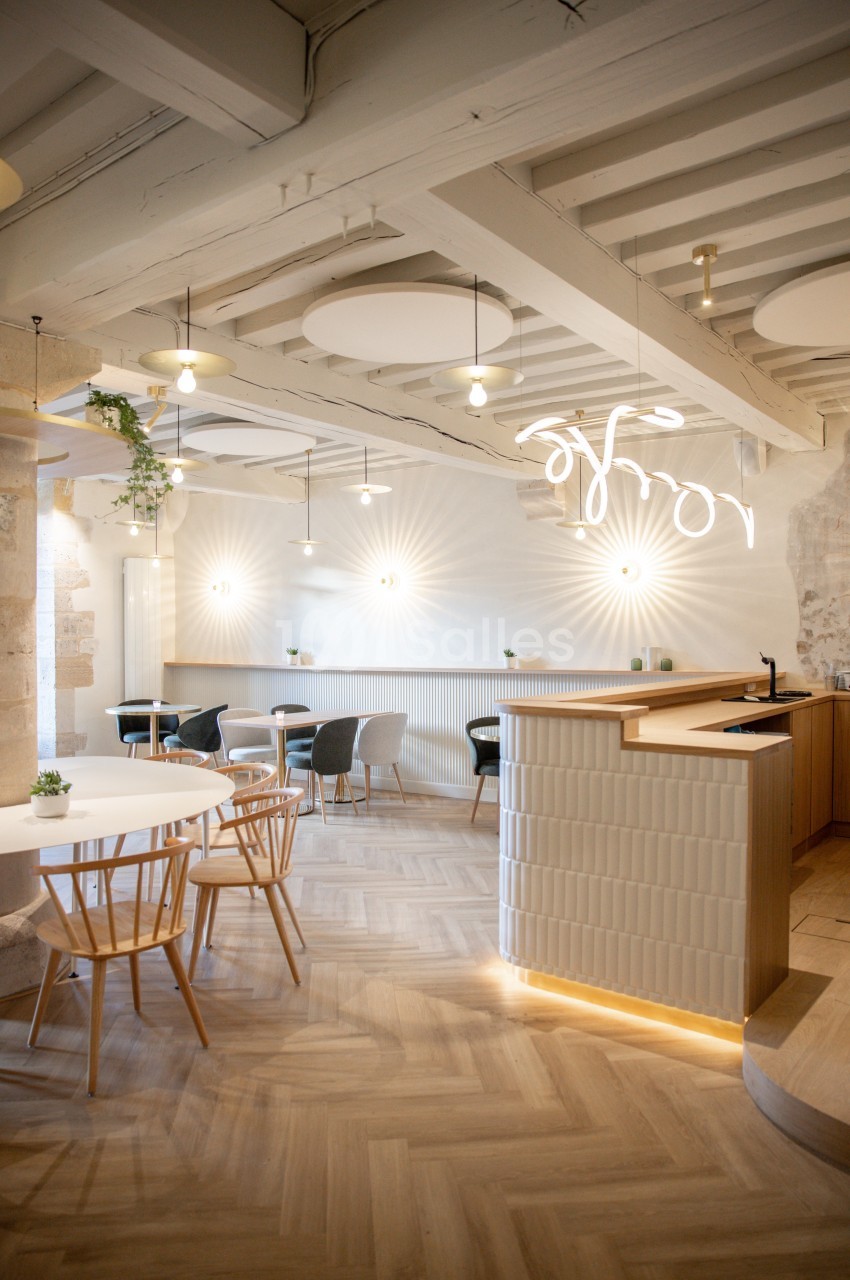 Intérieur lumineux d'un café moderne avec des murs en pierre, des tables en bois clair et un éclairage suspendu.