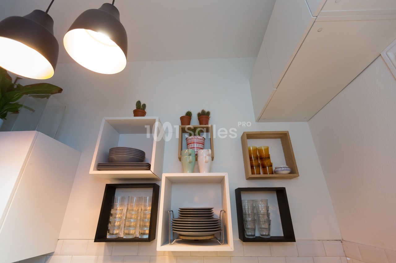 Étagères murales avec vaisselle, verres et plantes en pot dans une cuisine lumineuse au design moderne.