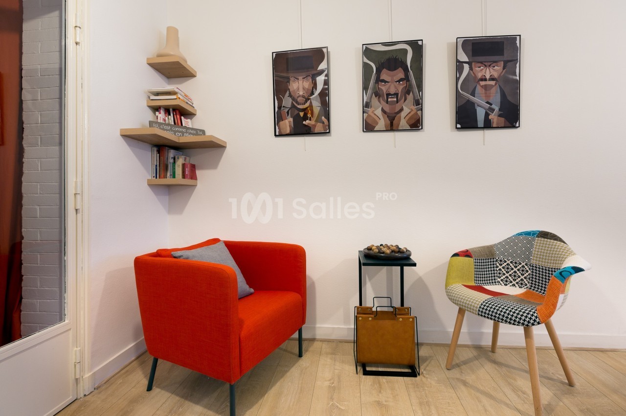 Deux fauteuils colorés, une table basse et des étagères murales dans un salon décoré de portraits encadrés.