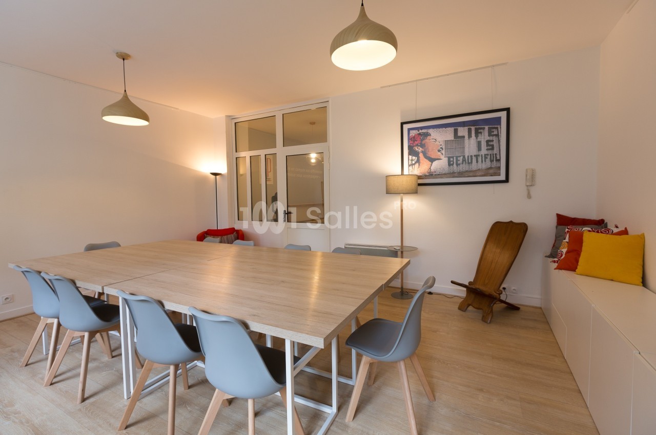 Salle de réunion lumineuse avec grande table en bois, chaises grises, éclairage suspendu et décoration murale.