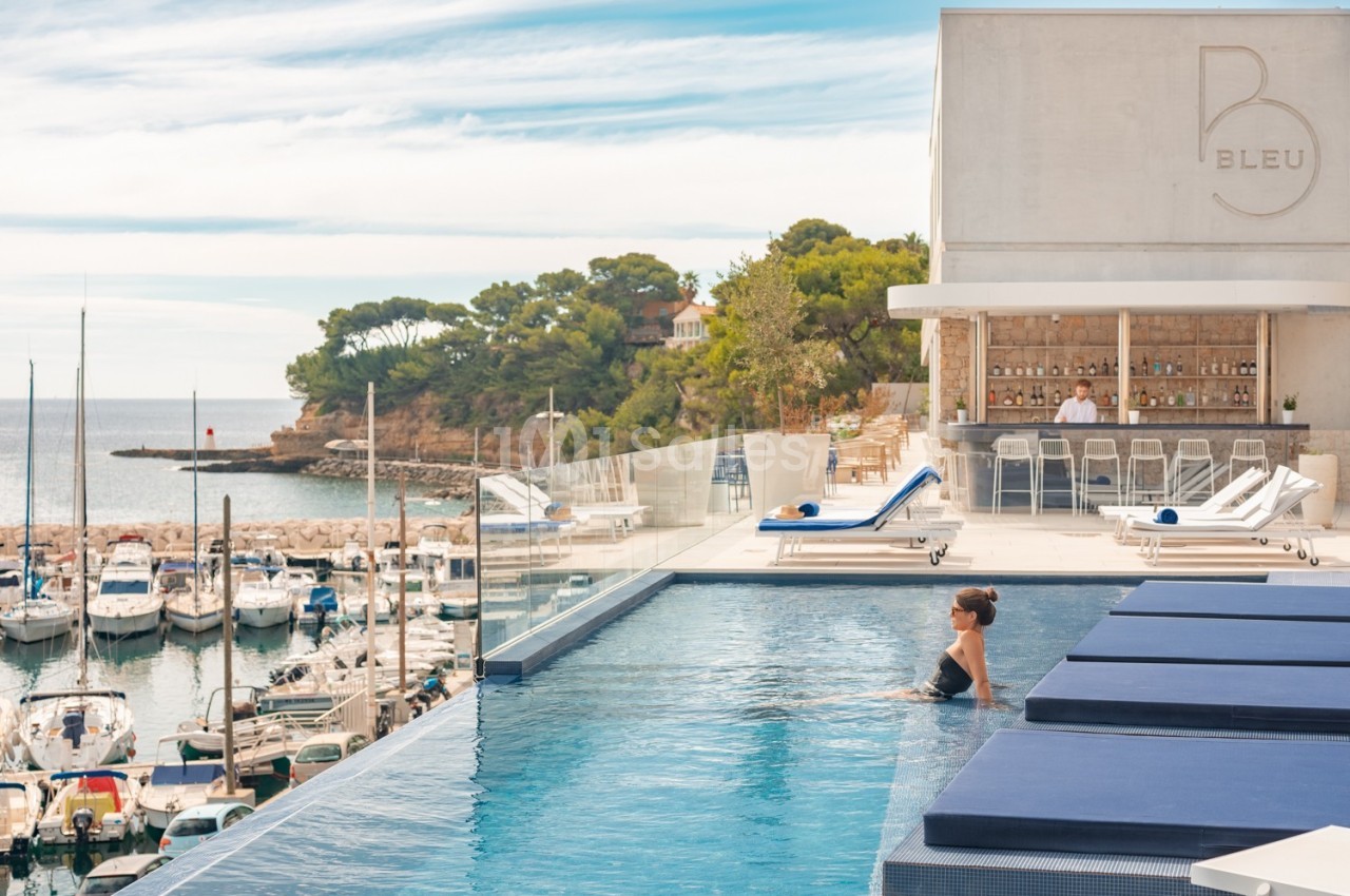 Piscine à débordement surplombant un port de plaisance, avec un bar en arrière-plan et vue sur la mer.
