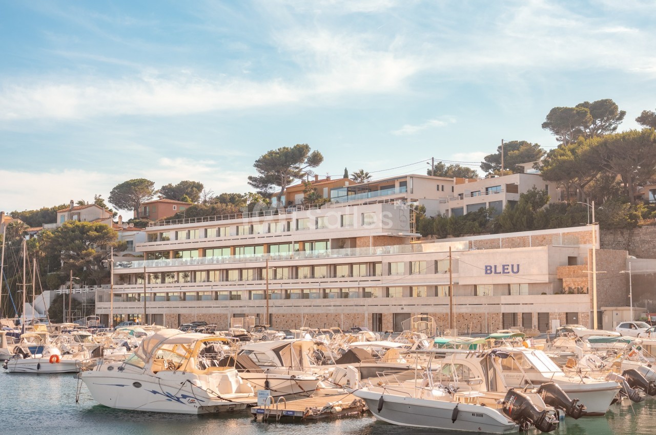 Vue d'un port de plaisance avec des bateaux amarrés devant un bâtiment moderne entouré de végétation.