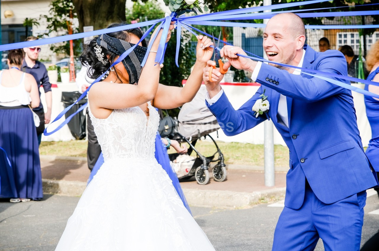 Un couple en tenue de mariage découpe des rubans bleus lors d'une célébration en extérieur.