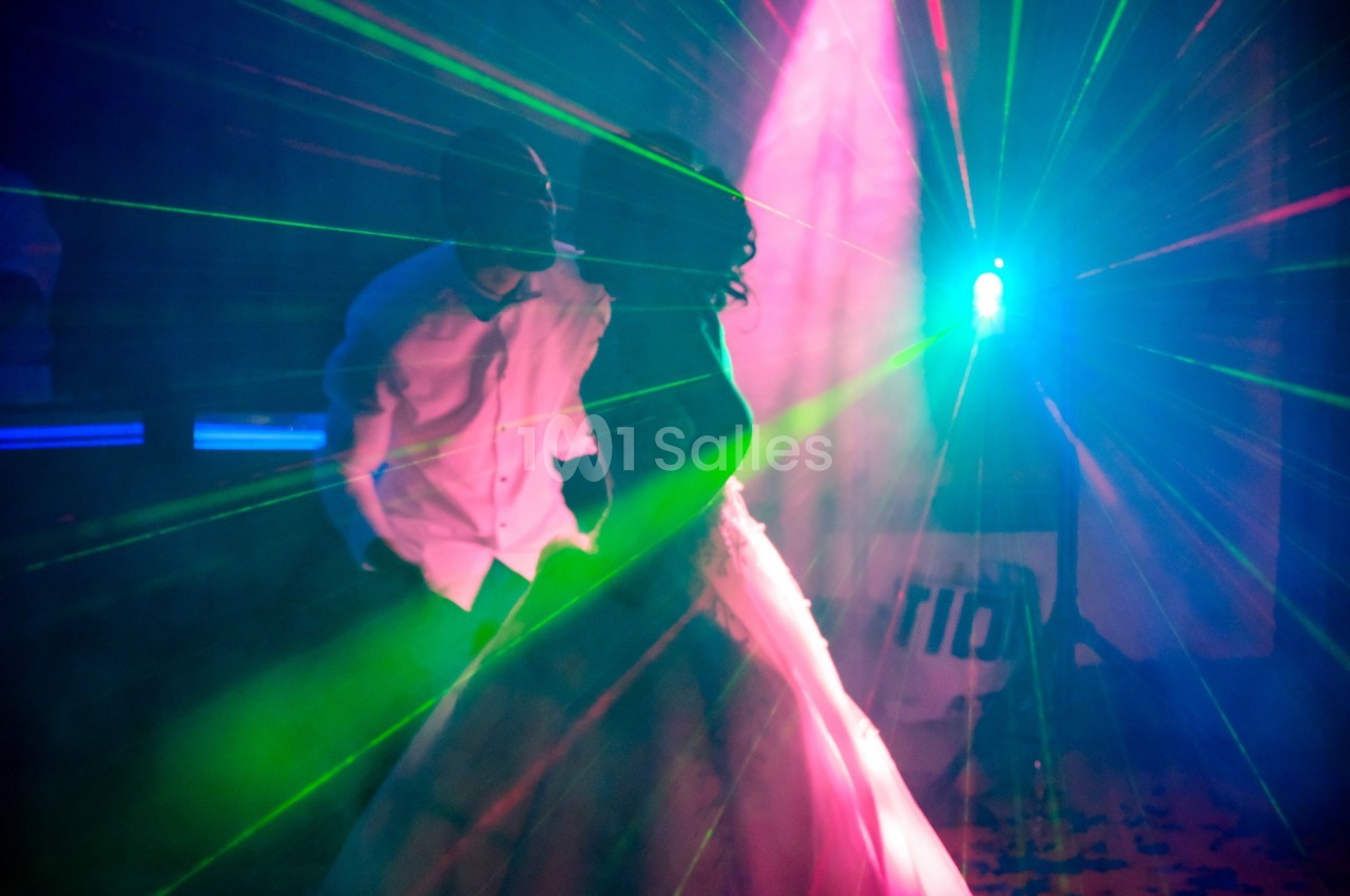 Un couple danse sous des lumières colorées et des faisceaux laser dans une ambiance festive.