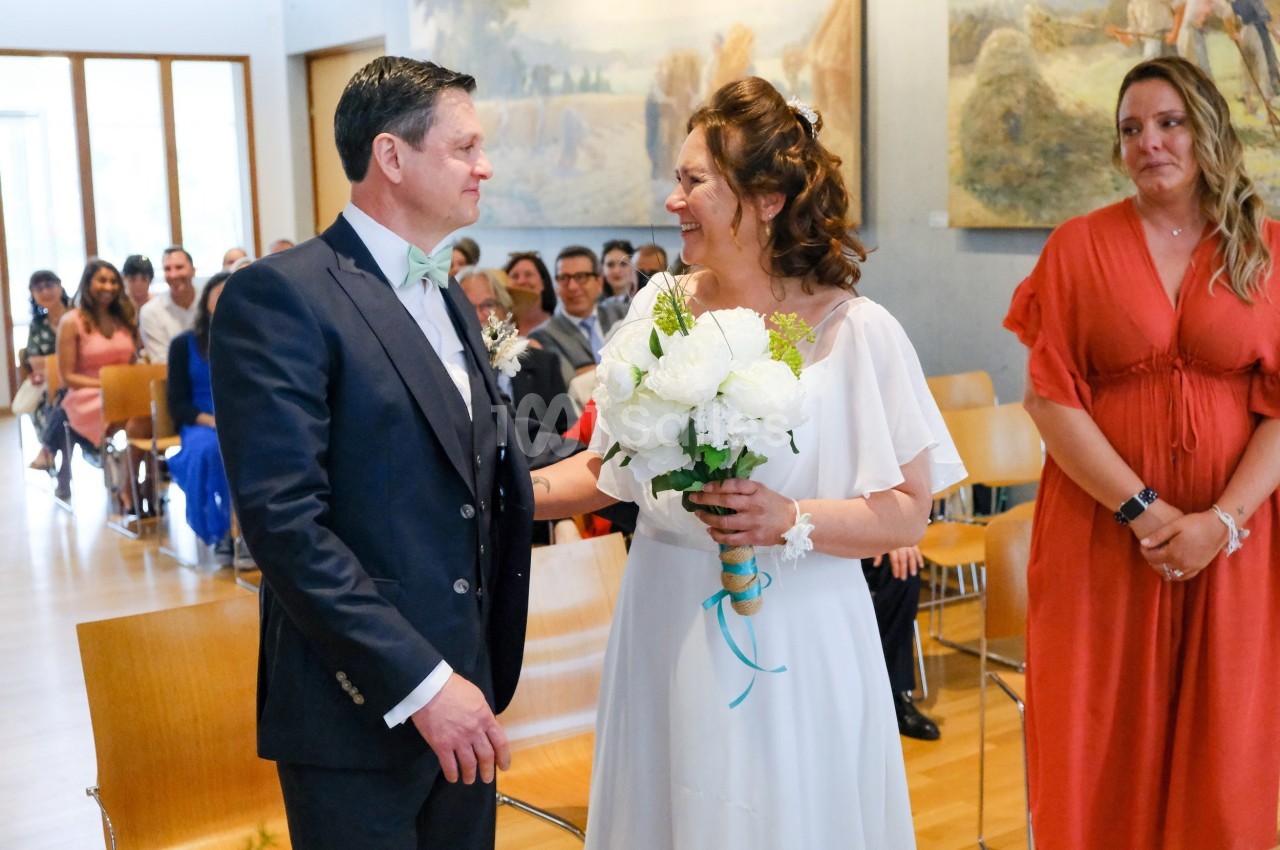 Un couple se regarde avec émotion lors d'une cérémonie de mariage, entouré d'invités assis dans une salle lumineuse.
