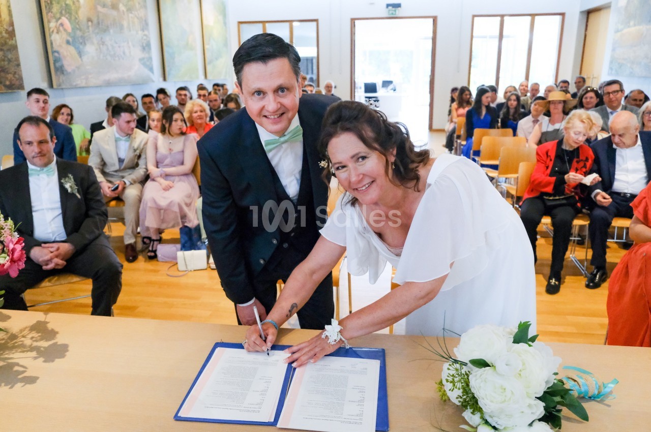 Un couple signe des documents officiels lors d'une cérémonie de mariage, entouré d'invités assis.