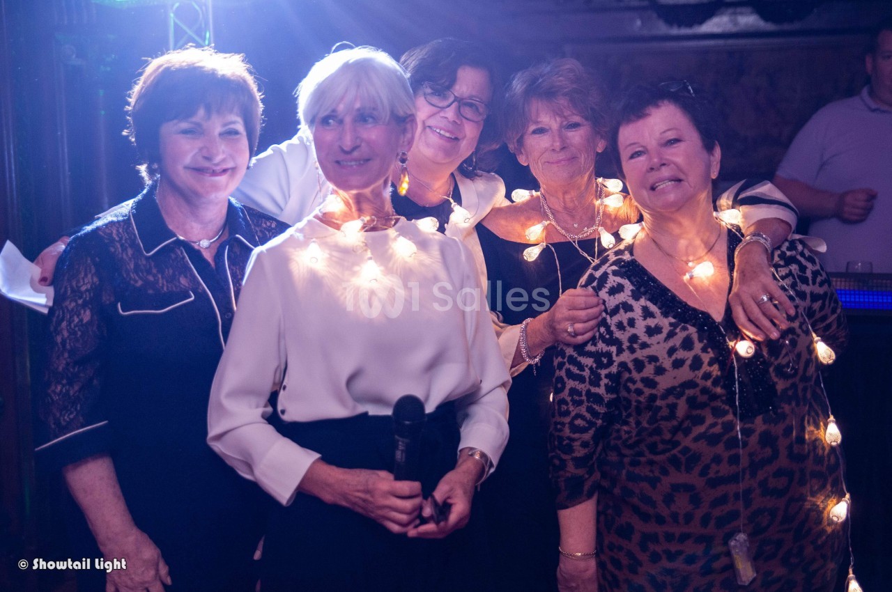 Cinq femmes souriantes posent ensemble, certaines portant des guirlandes lumineuses autour du cou.