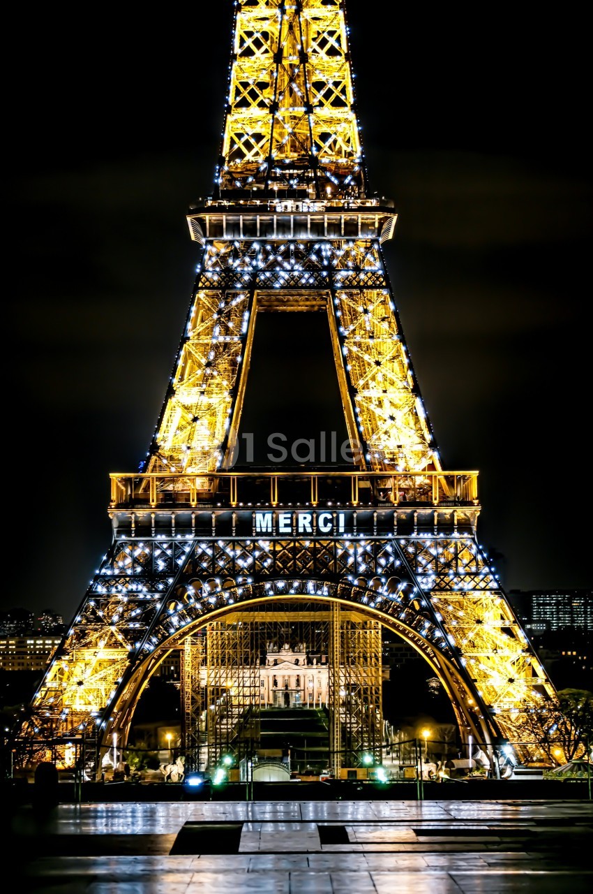 Tour Eiffel illuminée de nuit avec le mot ’MERCI’ affiché, et le Trocadéro visible en arrière-plan.