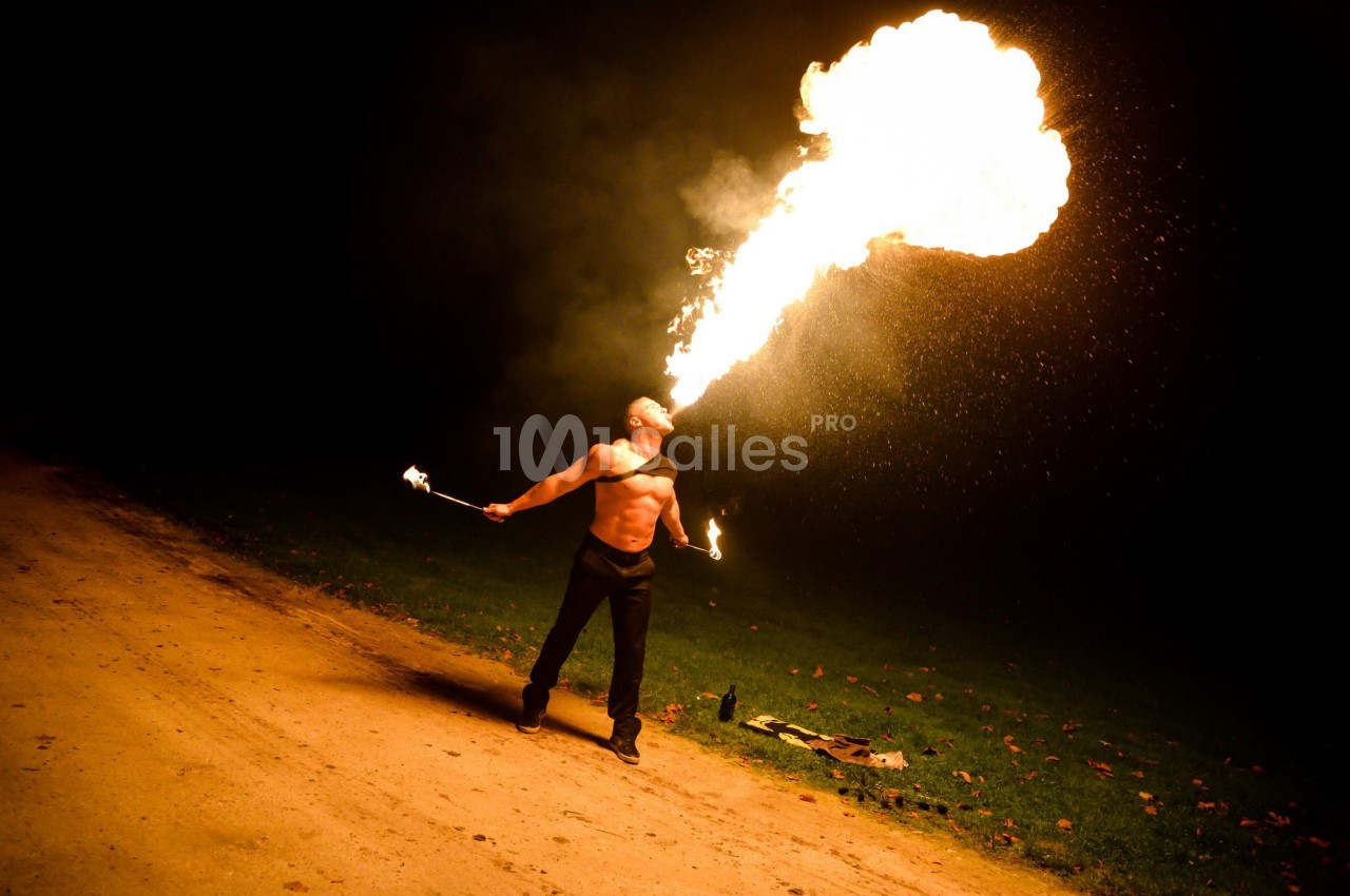 Un homme crache une grande flamme dans l'obscurité, tenant des torches enflammées dans chaque main.