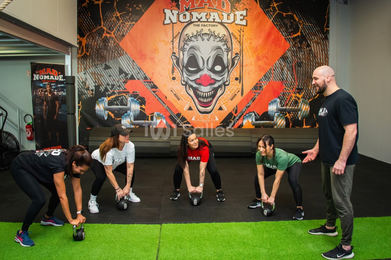 Quatre personnes s'entraînent avec des kettlebells sous la supervision d'un coach dans une salle de sport colorée.