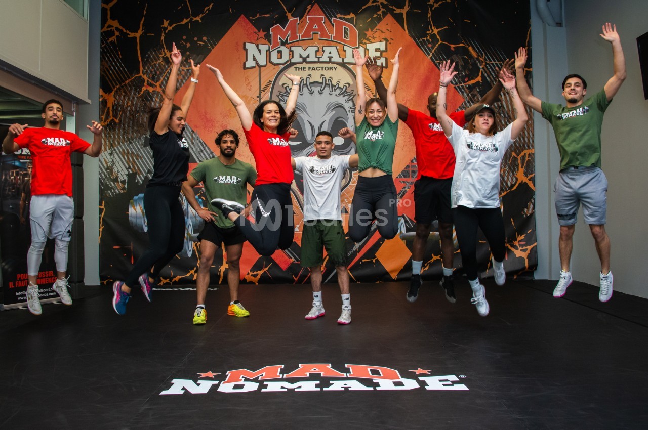 Groupe de personnes sautant en l'air dans une salle de sport avec un décor marqué ’Mad Nomade’ en arrière-plan.