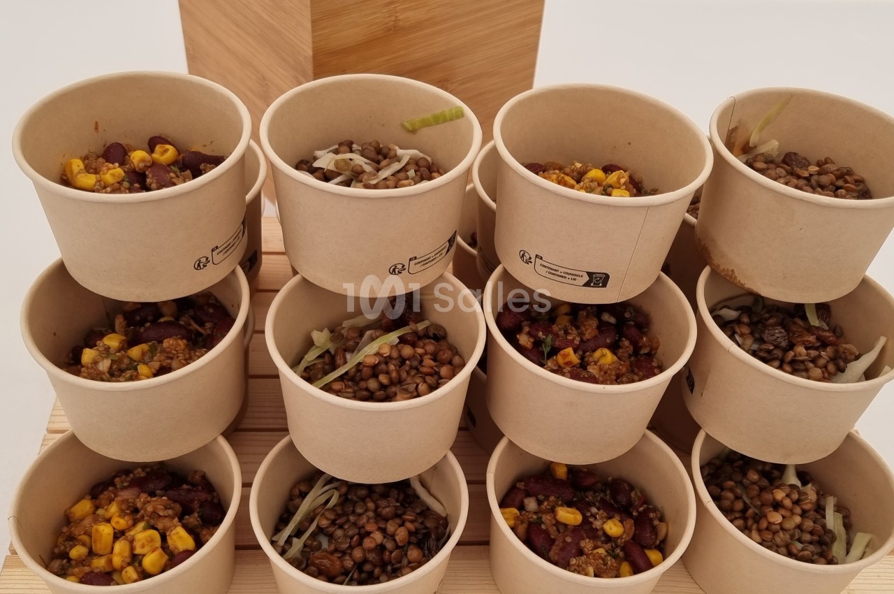 Coupes en carton remplies de lentilles, maïs et légumes, disposées en pyramide sur un support en bois.