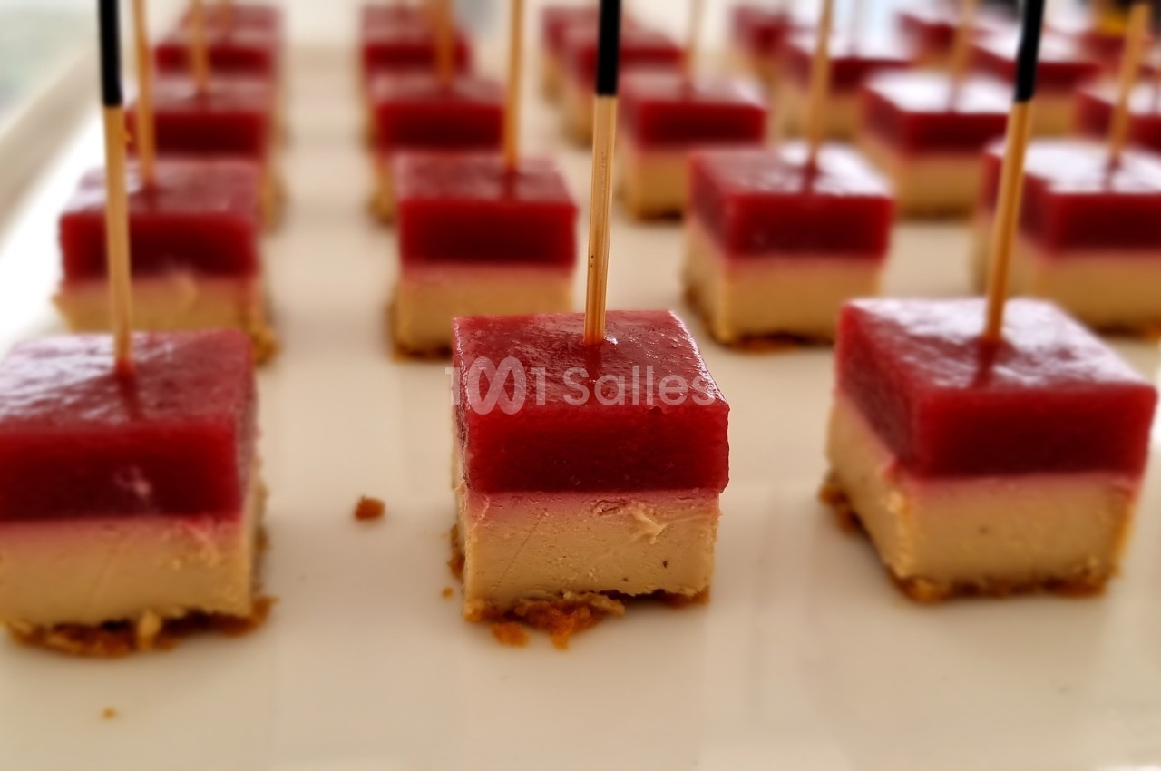 Carrés apéritifs composés de couches colorées, piqués avec des bâtonnets et disposés sur un plateau blanc.