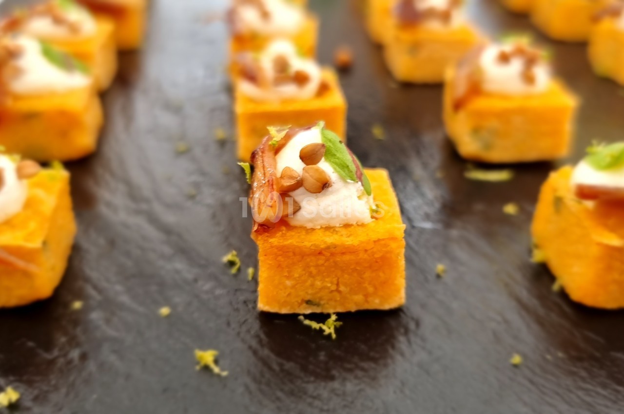 Bouchées apéritives sur ardoise, composées de cubes dorés garnis de crème, herbes et éclats croustillants.