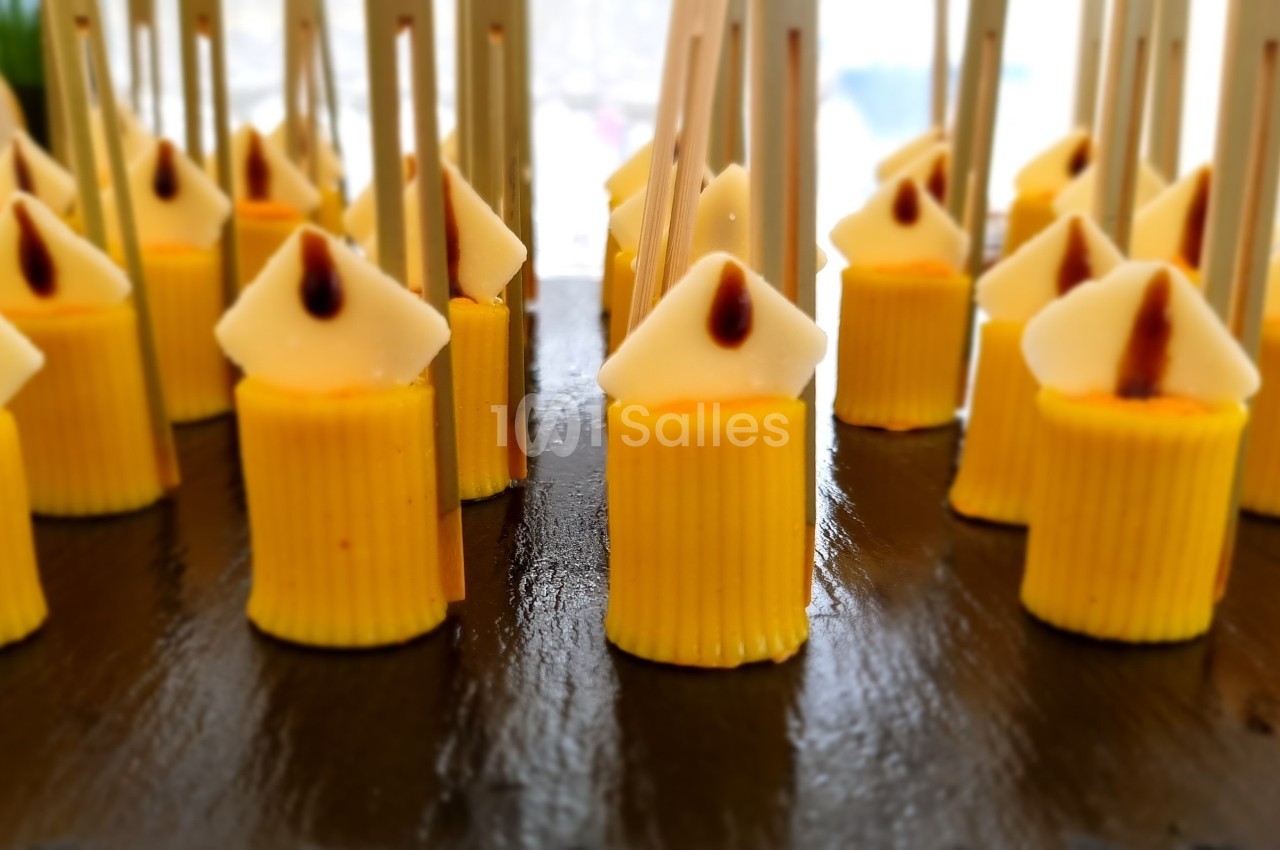 Petits desserts jaunes en forme de bougies avec des bâtonnets, disposés sur un plateau noir.