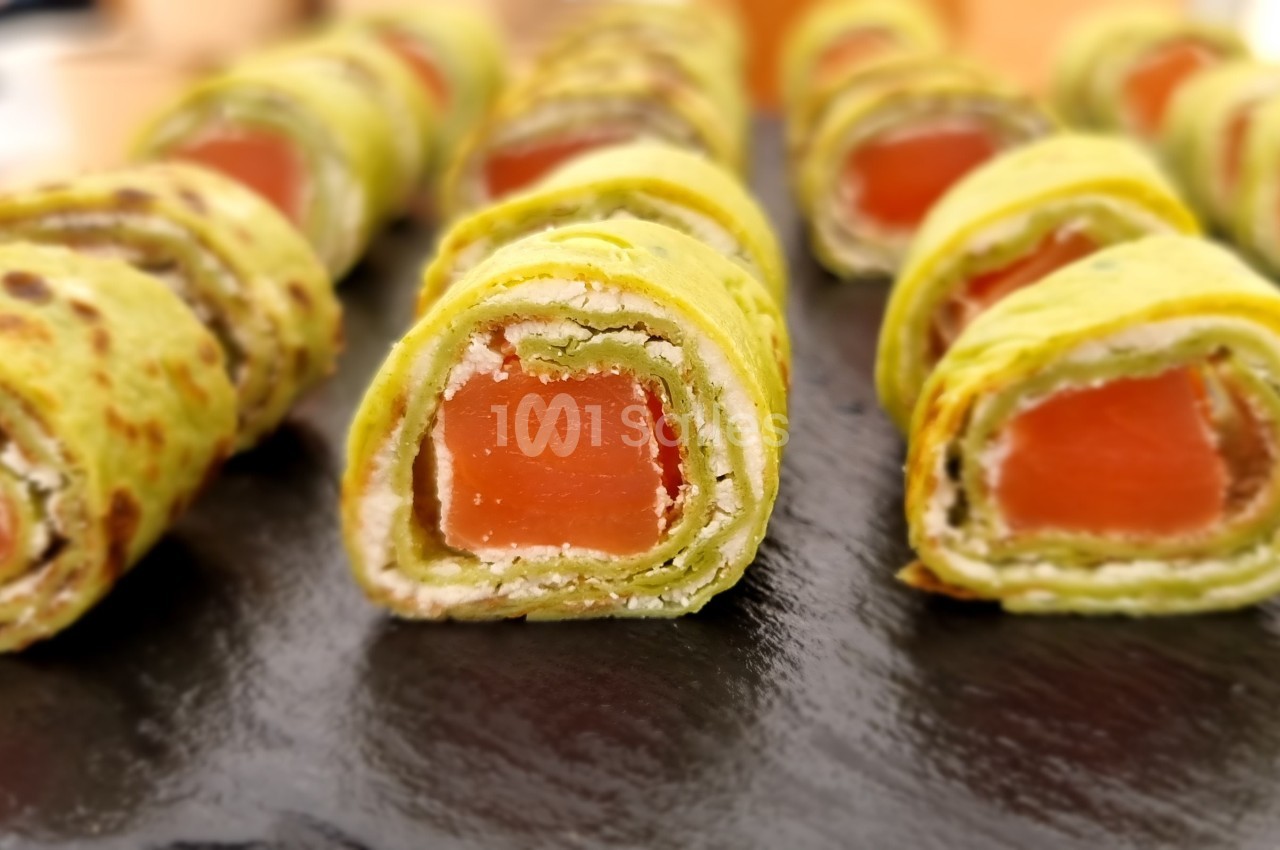 Roulés de crêpes vertes garnis de saumon et fromage frais, présentés sur une ardoise noire.