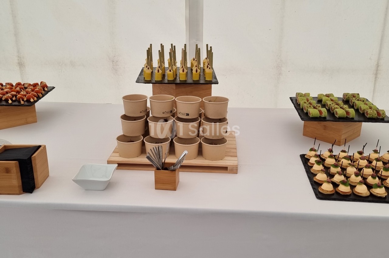 Buffet avec des amuse-bouches variés disposés sur des plateaux et supports en bois sur une nappe blanche.