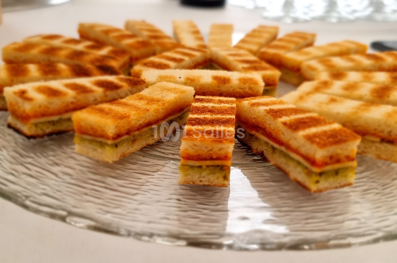 Assortiment de sandwichs grillés coupés en rectangles, disposés en cercle sur une assiette en verre.