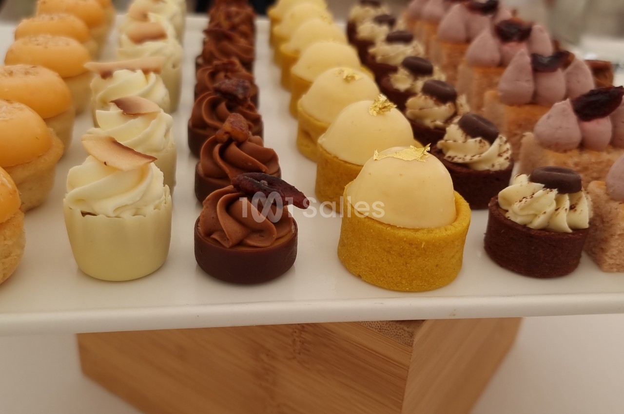 Plateau de mignardises variées disposées en rangées, comprenant des pâtisseries miniatures colorées et décorées.