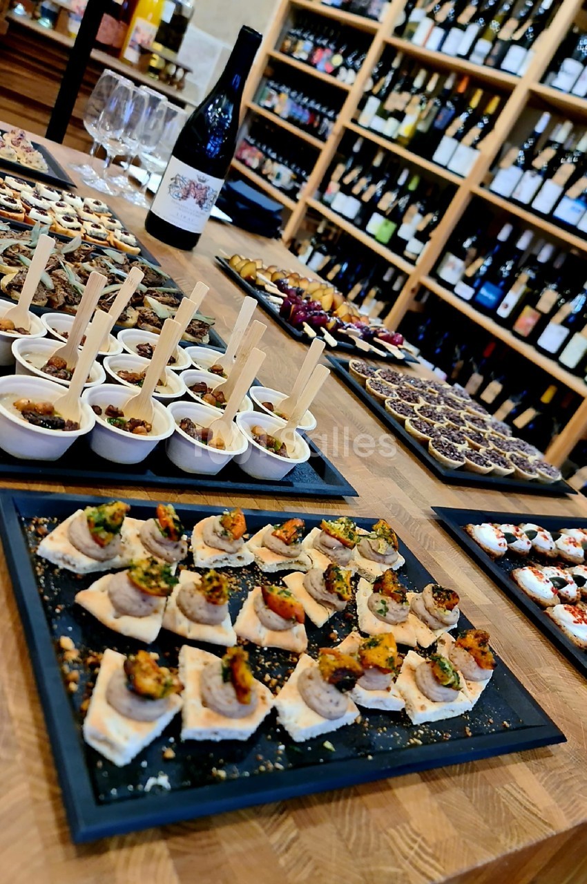 Plateau de tapas variés disposés sur une table en bois, avec des bouteilles de vin en arrière-plan.