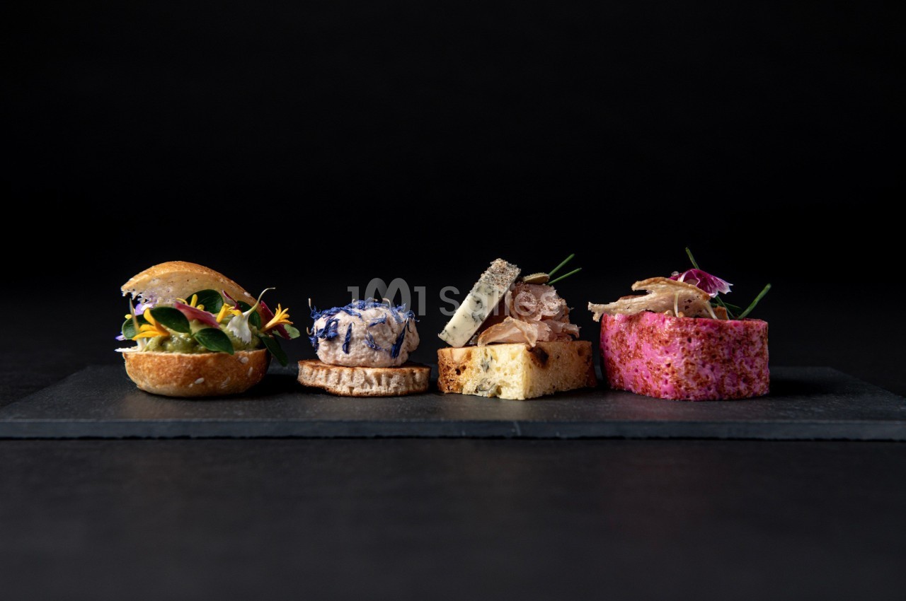 Assortiment de bouchées gastronomiques variées disposées sur une ardoise noire, avec un fond sombre.