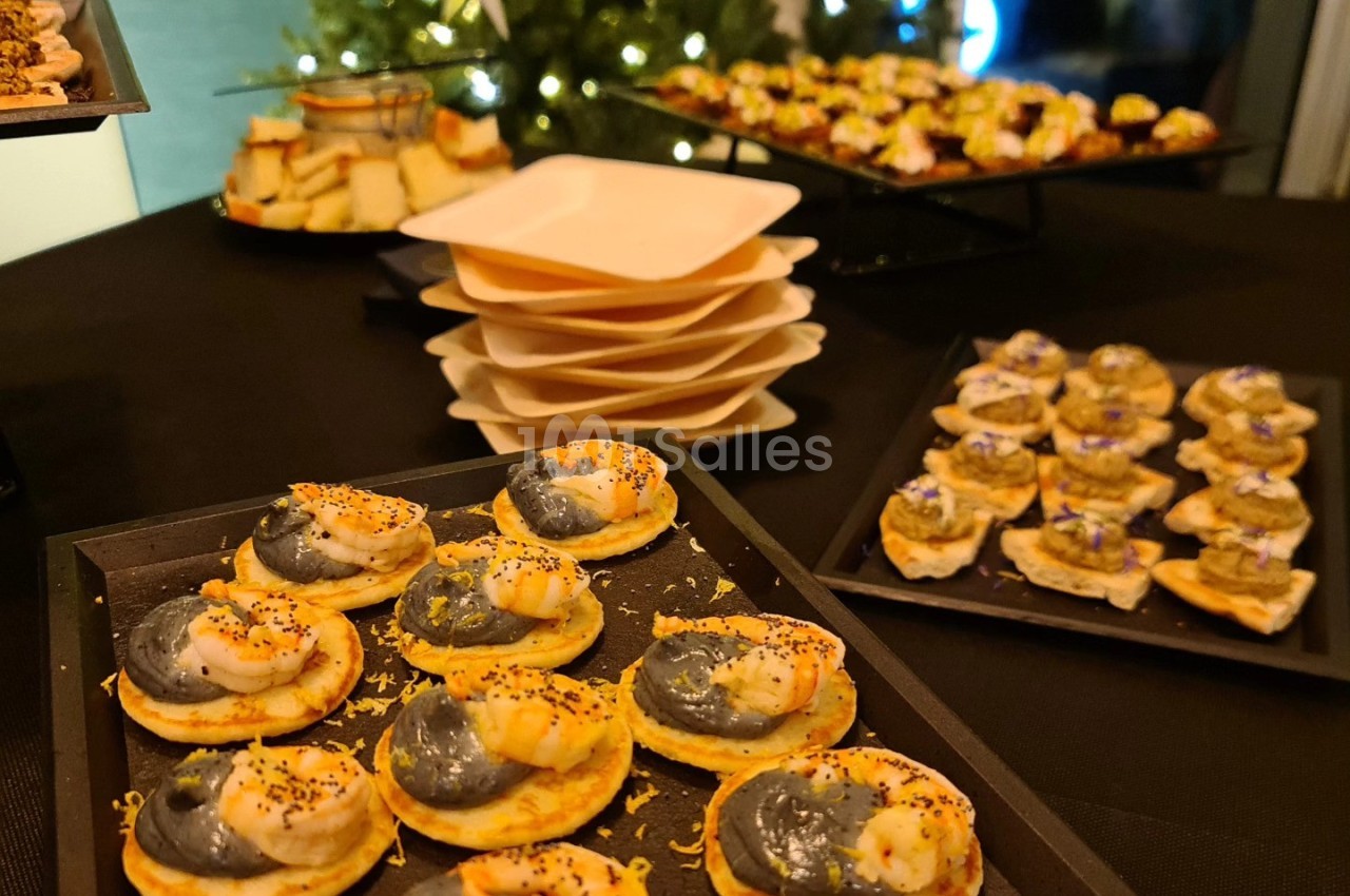 Plateaux de bouchées apéritives variées, dont des tartelettes garnies de crevettes, devant un sapin illuminé.