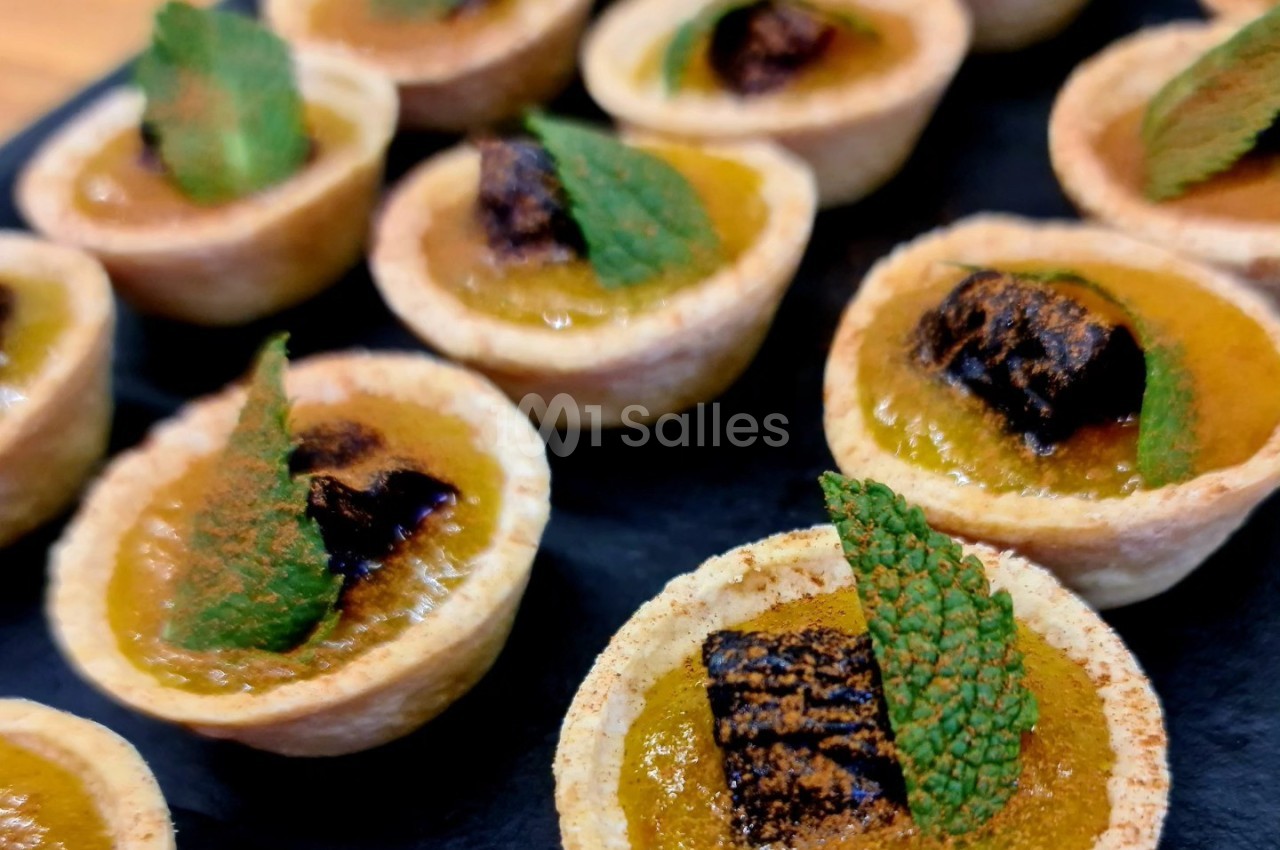 Petites tartelettes garnies de crème orange, décorées de feuilles de menthe et morceaux de chocolat, sur un plateau noir.